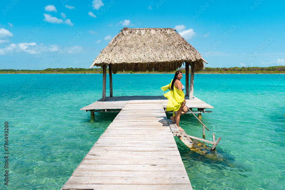 Chica joven en muelle en traje de baño amarillo de vacaciones bajando escalones a la laguna de bacalar - obrazy, fototapety, plakaty 