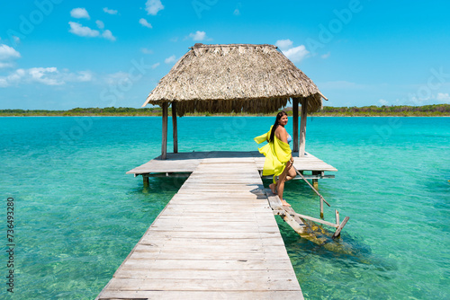Chica joven en muelle en traje de baño amarillo de vacaciones bajando escalones a la laguna de bacalar photo