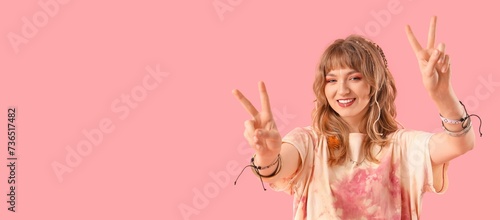 Female hippie showing peace gesture on pink background with space for text photo