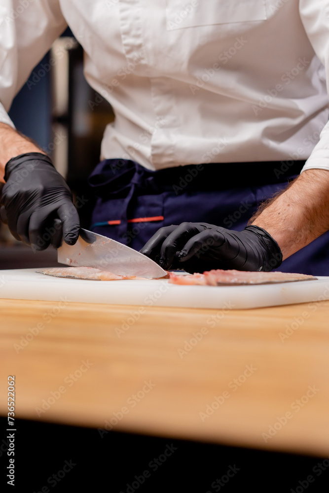 close-up of a chef cook in a professional kitchen cutting fish with knife before cooking