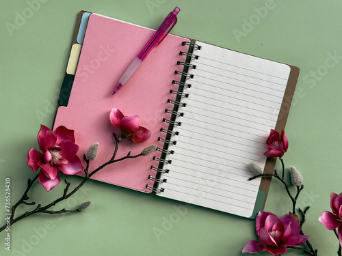 фотографія A pink notebook, with its pages neatly bound, is placed at the center of the frame with a pen lying on top of it