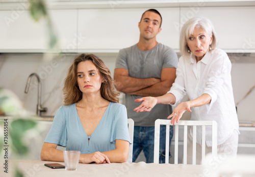 Adult man and elderly woman during family quarrel with adult woman in kitchen © JackF