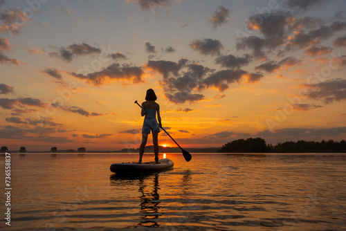 silhouette of woman on inflatable SUP board and paddling through shining water surface. aesthetically wide shot. Freedom happy female at sunset on a lake