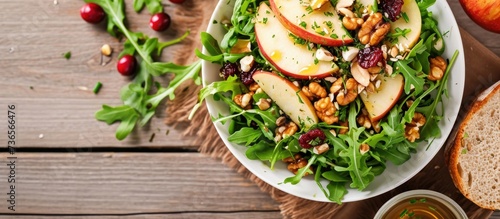 Green apple salad with rocket, oat granular, dried cranberry, and cashew nut in white dish on wooden table. Oil vinegar dressing, side dish. Two rocket leaves for decoration.