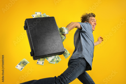 Excited man with roguish grin running away fast carrying a briefcase overstuffed with euro cash, a fun concept for money, winning or wealth, with bright yellow background photo
