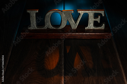 Metal Sign of the Word Love, on a Wooden Table and backlit with coloured light.