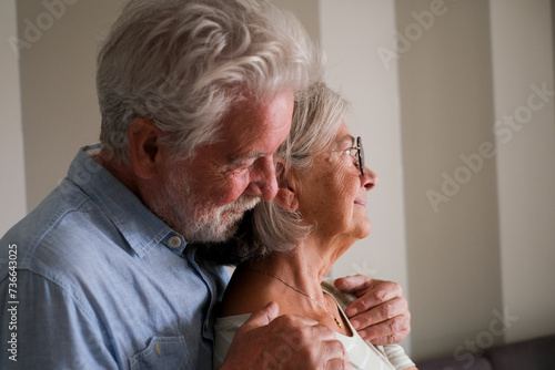 One senior man hug senior lady from behind to love and protect. Elderly lifestyle life together people. Retired couple at home thinking. Romantic sene with male and female having care each other photo