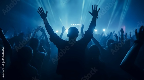 Rear view of crowd with arms outstretched at night club concert, blue red light background