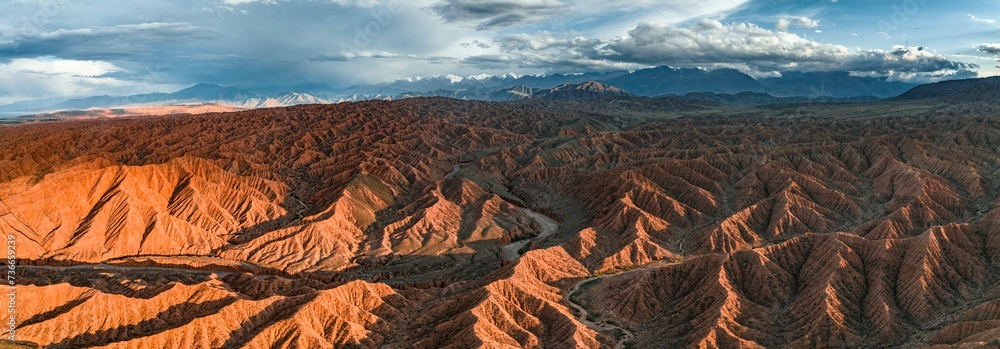 Tianshan Mountains Rivers River bed runs through a landscape of eroded hills, badlands at sunset ...