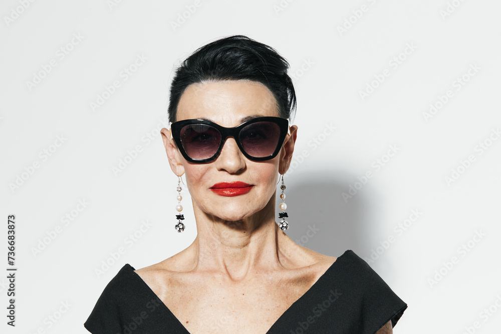 Elegant woman with black hair and red lipstick standing in front of white wall, wearing black dress and red earrings Elegant woman with black hair and red lipstick standing in front of white wall, wearing black dress and red earrings