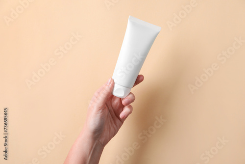 Woman with tube of hand cream on beige background, closeup