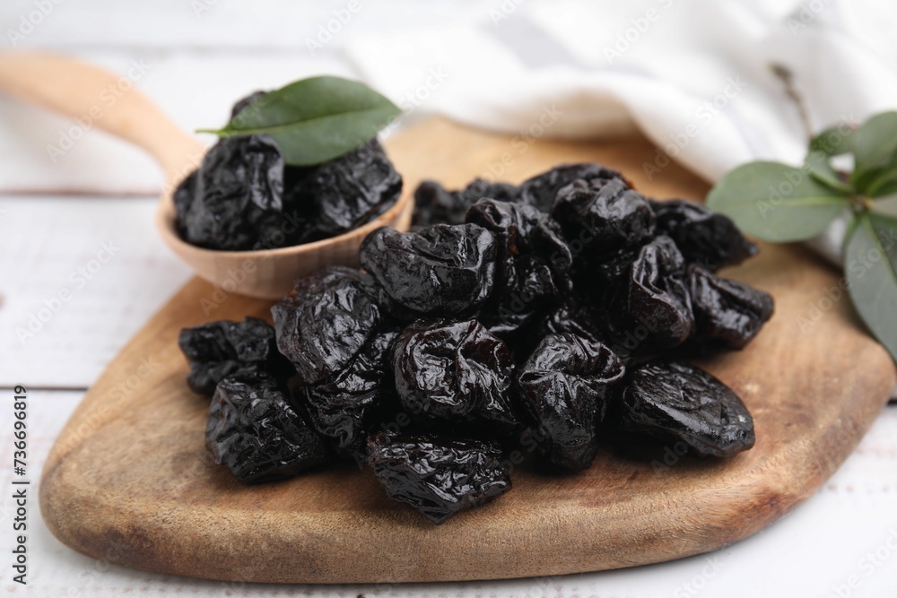 Spoon with tasty dried prunes and green leaves on light wooden table, closeup Spoon with tasty dried prunes and green leaves on light wooden table, closeup