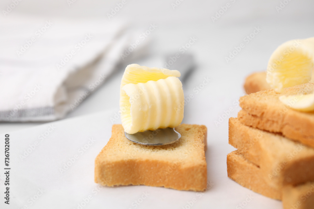 Tasty butter curls, knife and pieces of dry bread on white table, closeup