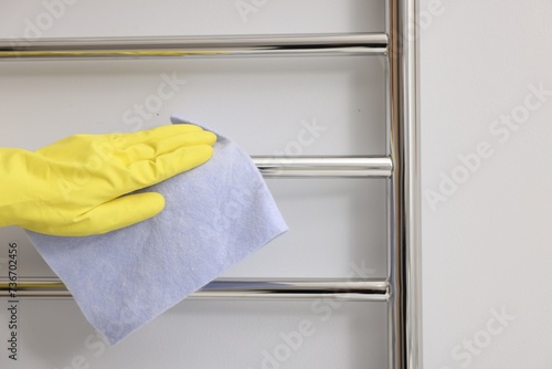 Woman cleaning heated towel rail with rag indoors, closeup