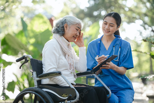 Compassionate Asian woman provides care to  elderly person in wheelchair outdoors. Engaging in physical therapy, happiness, encouraging positive environment for mature individuals with grey hair. © makibestphoto
