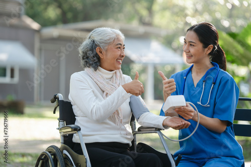 Compassionate Asian woman provides care to elderly person in wheelchair outdoors. Engaging in physical therapy, happiness, encouraging positive environment for mature individuals with grey hair.