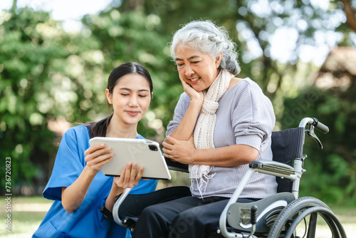 Compassionate Asian woman provides care to elderly person in wheelchair outdoors. Engaging in physical therapy, happiness, encouraging positive environment for mature individuals with grey hair.