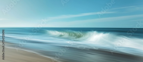 A hazy image capturing the fluid movement of waves crashing on a sandy beach under a cloudy sky with the horizon in the background