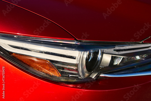 Closeup of the chrome headlights on a brilliant red colored car. © Wirestock