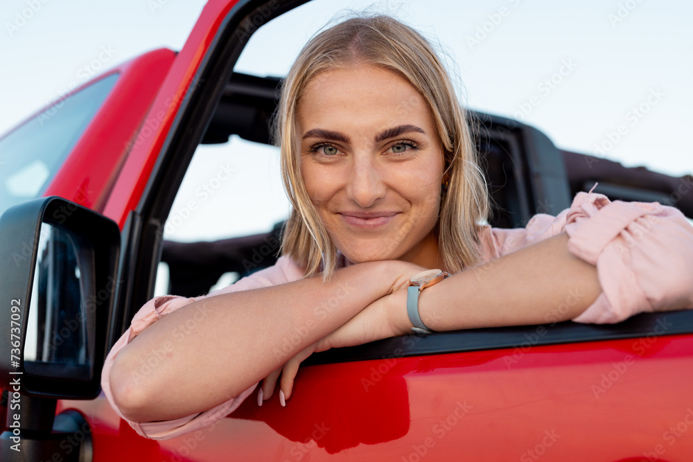 Young Caucasian woman leans on a red car door on a road trip Young Caucasian woman leans on a red car door on a road trip