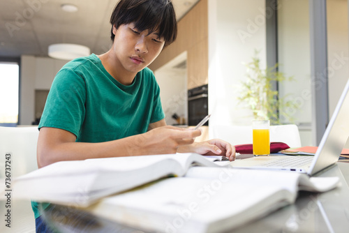 Teenage Asian boy studies intently at home, surrounded by books photo