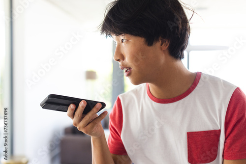 Teenage Asian boy speaks into a phone at home, with copy space photo