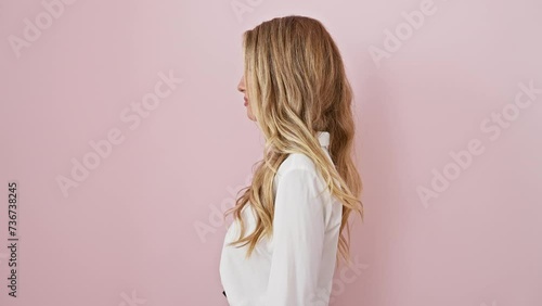 Confident young blonde woman in a relaxed natural pose, smiling cheekily while looking off to the side - isolated over pink backdrop photo