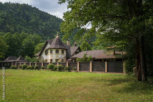 View of a cottage in the village of Guzeripl against the backdrop of the Caucasus Mountains on a sunny summer day with clouds, Guzeripl, Republic of Adygea, Russia photo