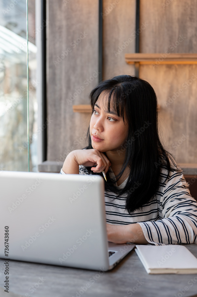 Woman is looking out the window and contemplating something while working remotely at a coffee shop. Woman is looking out the window and contemplating something while working remotely at a coffee shop.