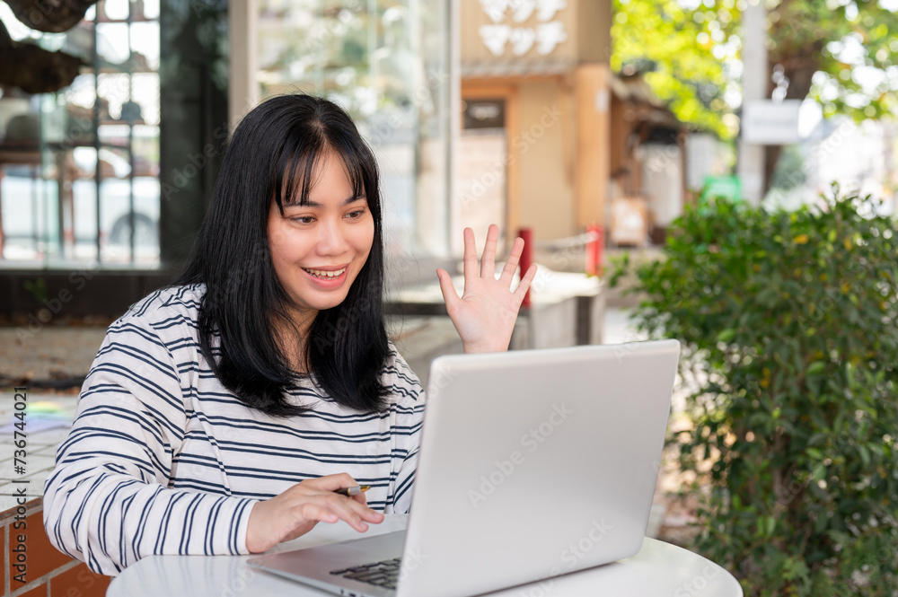 A positive Asian woman is having an online meeting with her team, working remotely at a cafe. A positive Asian woman is having an online meeting with her team, working remotely at a cafe.