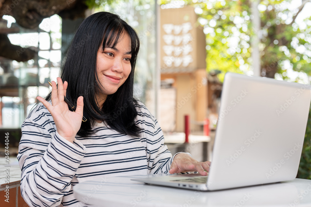 A positive Asian woman is having an online meeting with her team, working remotely at a cafe. A positive Asian woman is having an online meeting with her team, working remotely at a cafe.