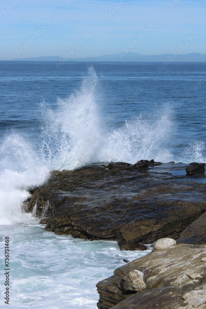 a rock that has some water crashing around it, next to the ocean a rock that has some water crashing around it, next to the ocean