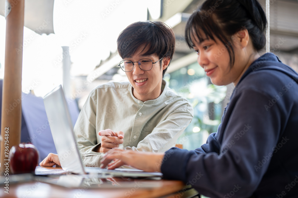 Two happy young Asian college students are discussing and working on a project in a cafe together. Two happy young Asian college students are discussing and working on a project in a cafe together.