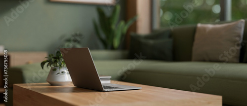 Close-up image of a laptop computer on a wooden coffee table in a modern living room in green color.