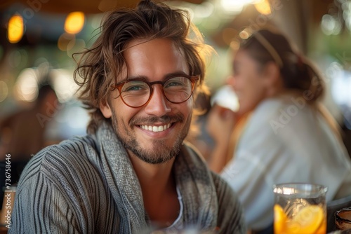 Handsome young man with glasses and a comfortable sweater smiling at a cafe