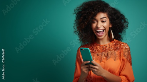 Joyful woman in orange dress with smartphone on teal background