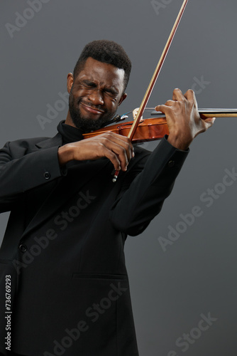 Elegant African American man in tuxedo playing the violin against a gray background, creating beautiful music