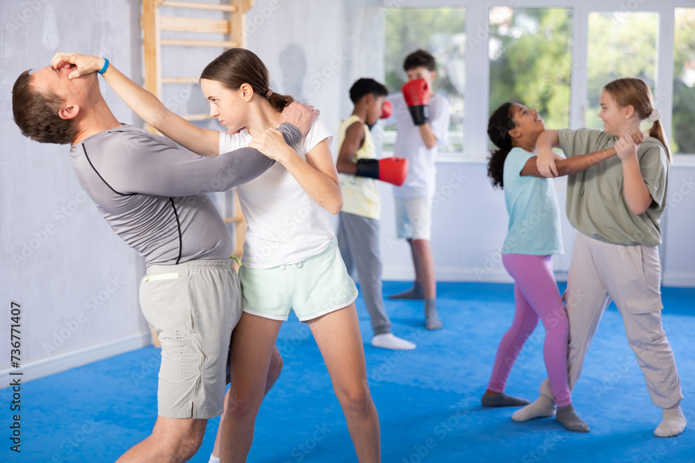 Fototapeta premium Coach man and girl training self-defense techniques in studio..