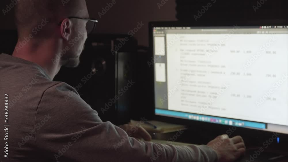 A Man In The Dark Sits In Front Of A Large Monitor. Works at the computer A Man In The Dark Sits In Front Of A Large Monitor. Works at the computer