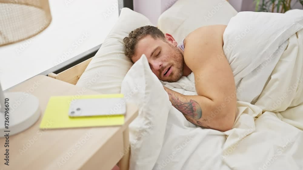 Bearded man waking up disoriented in a modern bedroom, reaching for his smartphone on the bedside table. Bearded man waking up disoriented in a modern bedroom, reaching for his smartphone on the bedside table.