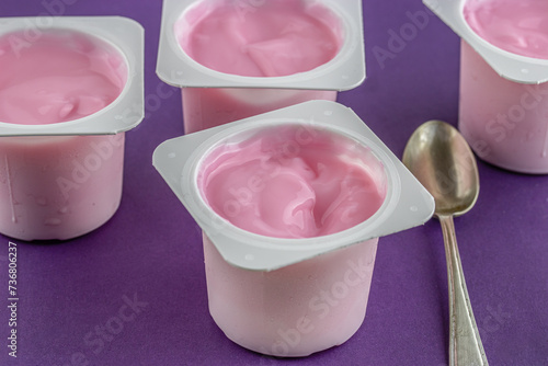 Pink yogurt cup with defocused cups on purple background
