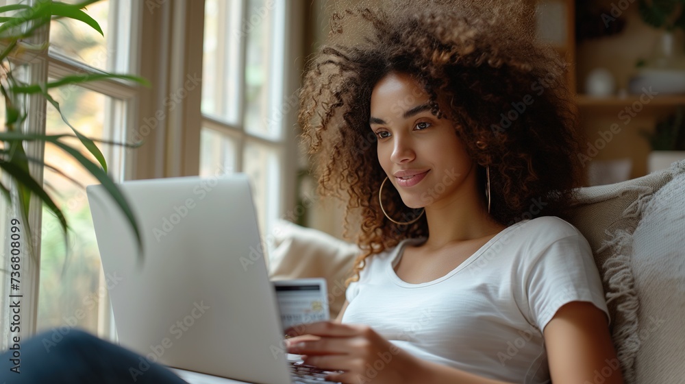 A curly woman sits at a laptop and makes purchases online at home, paying with a bank credit card. Shopping online, season of sales and discounts, best deals. Online store advertising A curly woman sits at a laptop and makes purchases online at home, paying with a bank credit card. Shopping online, season of sales and discounts, best deals. Online store advertising