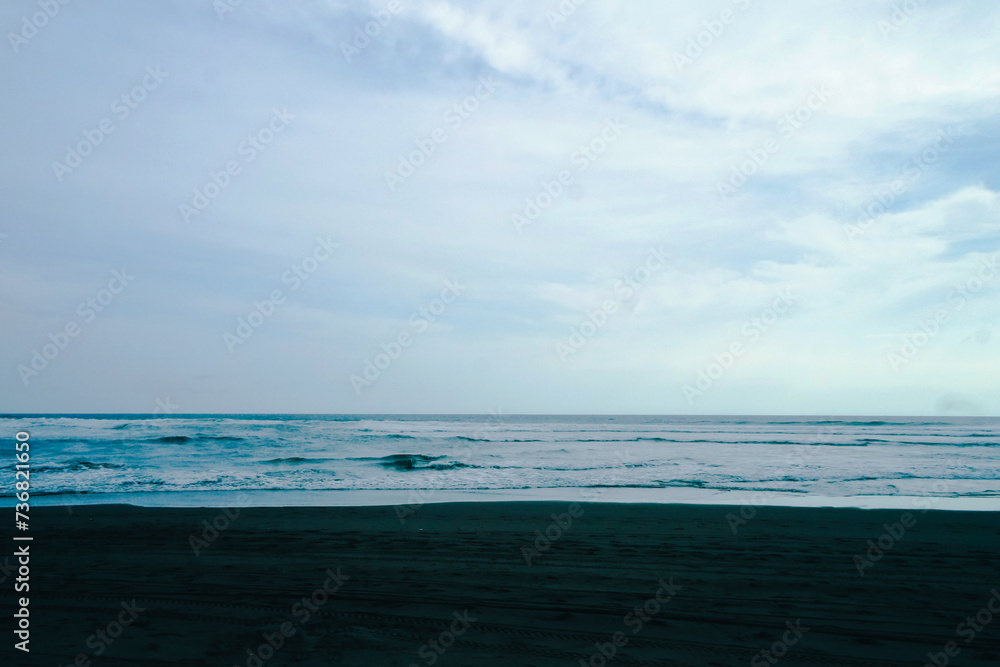 Beautiful beach with a blue sky and black sand and wavy waves