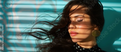 a close up of a woman's face with her hair blowing in the wind in front of a blue wall.
