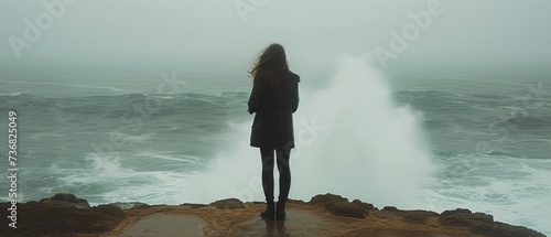 a woman standing on the edge of a cliff looking out at a large body of water on a foggy day. photo