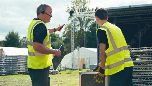 Male Production Team Moving Flight Case And Setting Up Outdoor Stage For Music Festival 