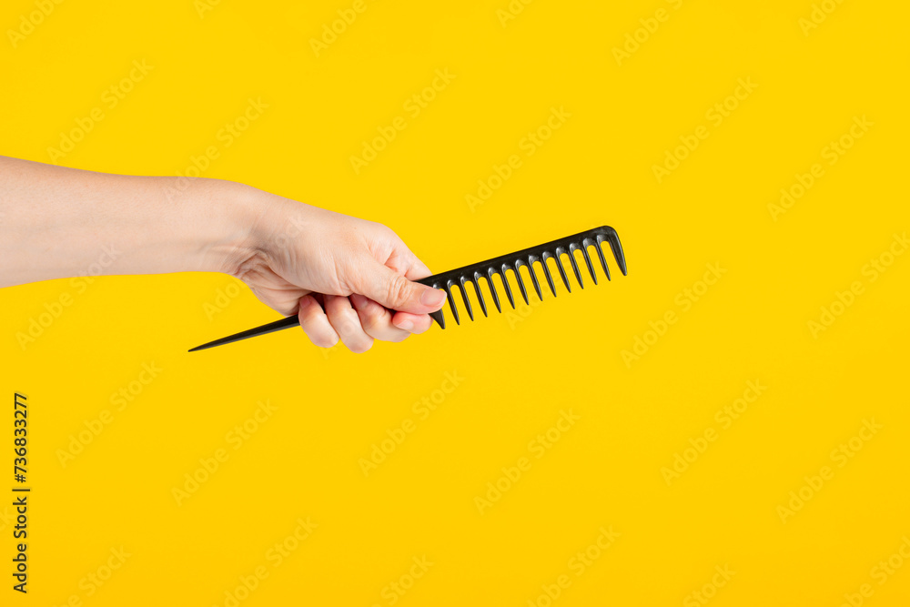 Naklejka premium Black hair comb in hand isolated on yellow background