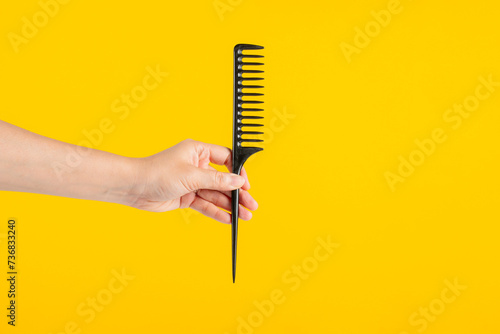 Black hair comb in hand isolated on yellow background