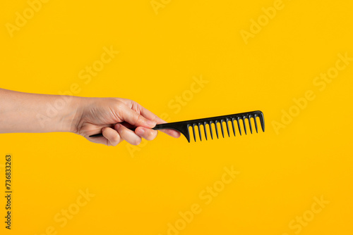 Black hair comb in hand isolated on yellow background photo