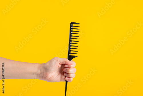 Black hair comb in hand isolated on yellow background